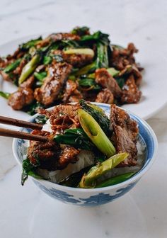 a bowl filled with meat and veggies on top of a white table next to chopsticks