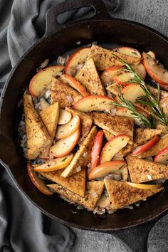 a skillet filled with chicken, apples and rice topped with fresh rosemary sprigs