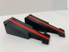 two pieces of black and red plastic sitting on top of a white table next to each other