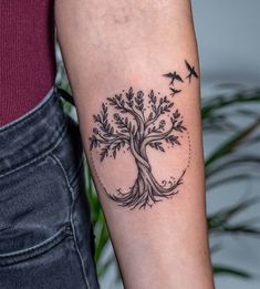 a woman's arm with a tree and birds tattoo on the left inner arm