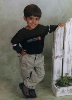 a young boy standing next to an old white fence with his hand on the rail