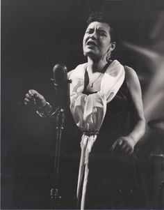 a black and white photo of a woman singing into a microphone