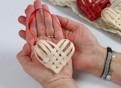 a person holding a heart shaped ornament in their hands with red ribbon around it