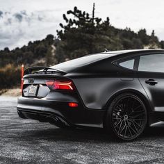 the rear end of a black sports car parked in a parking lot next to trees