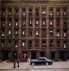 an old black car parked in front of a tall building with mannequins on the windows