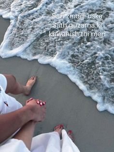 two people sitting on the beach with their feet in the sand