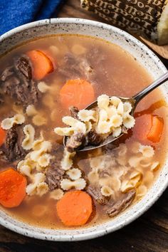 a bowl of beef and dumpling soup with carrots on the side next to a bag of bread