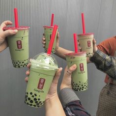 four people holding up green drinks with red straws