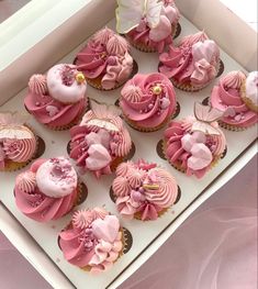 cupcakes with pink frosting and flowers in a white box on a table