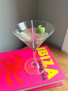 a martini glass with an olive in it on top of a pink book