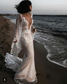 a woman standing on top of a beach next to the ocean wearing a white dress