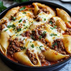 a skillet filled with pasta and meat covered in sauce, cheese and parsley