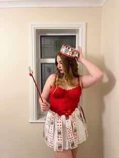 a woman in a red and white dress is holding a broom while standing next to a window