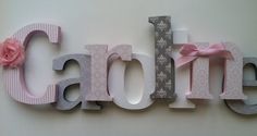 the word cake decorated with pink flowers and ribbon is displayed on a wall in front of a white background