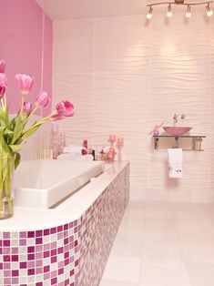 a bath room with a tub a sink and pink flowers in vases on the counter