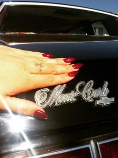 a woman's hand on the hood of a vintage car with nails painted red