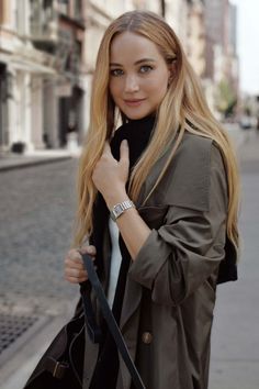 a woman is standing on the street with her hand in her pocket and looking at the camera