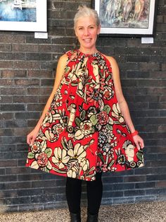 a woman standing in front of a brick wall wearing a dress with flowers on it