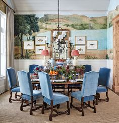 a dining room table with blue chairs and a painting on the wall in the background