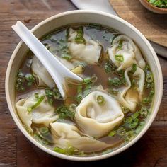 a bowl of soup with dumplings and green onions in it on a wooden table