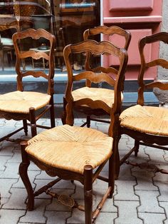 four wooden chairs sitting next to each other on a brick floor in front of a store