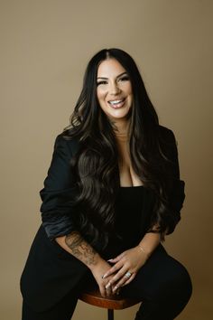 a woman sitting on top of a wooden stool with her arms crossed and smiling at the camera