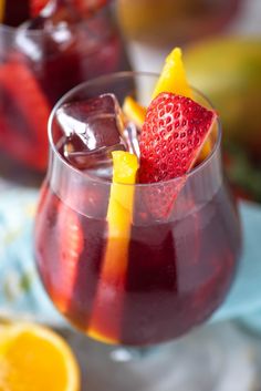 two glasses filled with liquid and fruit garnished with oranges, strawberries, and lemon wedges