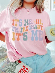 a woman wearing a pink shirt with the words it's me, i'm pregnant and it's me