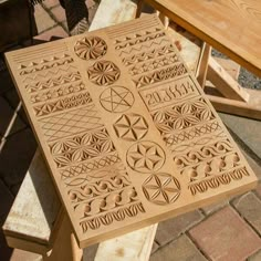 a wooden table with carved designs on the top and bottom, sitting on brick pavers