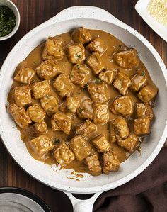 a white bowl filled with meat and gravy on top of a wooden table