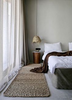 a bed room with a neatly made bed next to a window and a rug on the floor