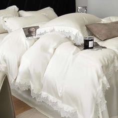 a bed with white comforters and pillows on top of it, next to a table