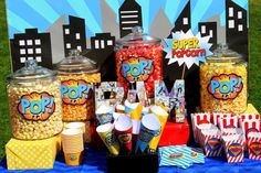 a table topped with lots of popcorn next to two large containers filled with candy and other snacks