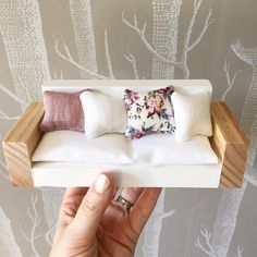 a hand holding a miniature couch with pillows on it