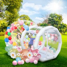 an inflatable bubble filled with balloons on the grass next to a woman and child