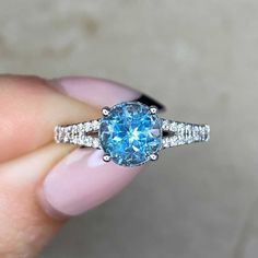 a woman's hand holding an engagement ring with a blue and white diamond in it