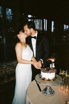 a newly married couple kissing in front of a wedding cake with lit candles on it