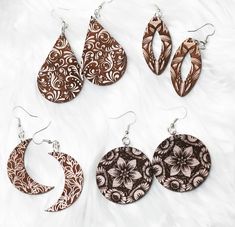 four different styles of earrings on a white surface with furnishing and fabric in the background