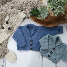 three knitted sweaters and a teddy bear are on the floor next to a potted plant