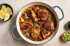 a pan filled with meat and vegetables next to some lemon wedges on the side