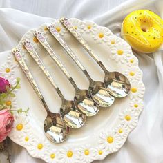 four silver spoons sitting on top of a white plate next to flowers and a yellow vase