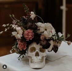 a skull with flowers in it sitting on a white table cloth covered tablecloth,