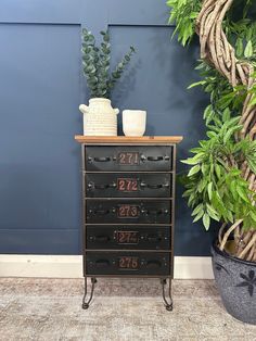 a black dresser with three drawers next to a potted plant