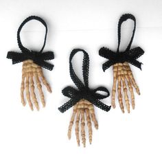 three small hand puppets with black ribbons tied to them on a white surface, one is made out of wood and the other has two hands that have bones attached