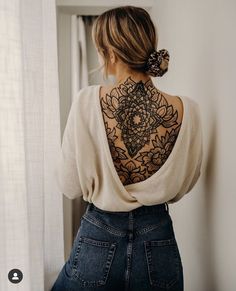 a woman with a tattoo on her back standing in front of a window and looking out the window