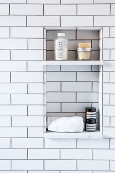 a white shelf with some bottles and jars on it in front of a brick wall