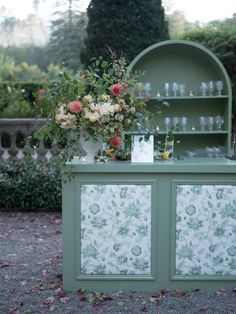 a green cabinet with flowers and candles on it's top, next to a vase filled with flowers