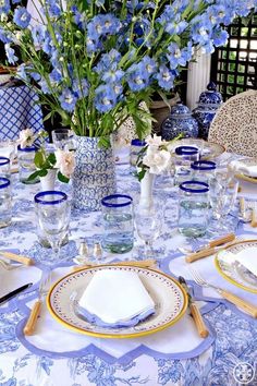 a blue and white table setting with flowers in vases on the centerpiece, plates and utensils