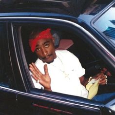 a man sitting in the passenger seat of a car wearing a red bandana and holding his hand up