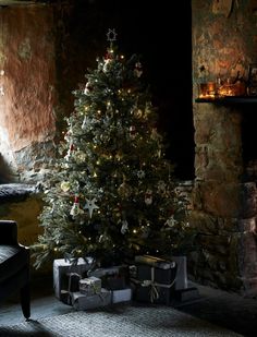 a lit christmas tree in a living room next to a fireplace with presents under it